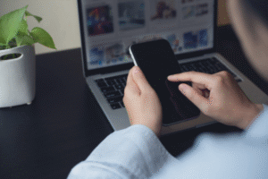 A mobile phone being held above an open laptop with social media images on screen