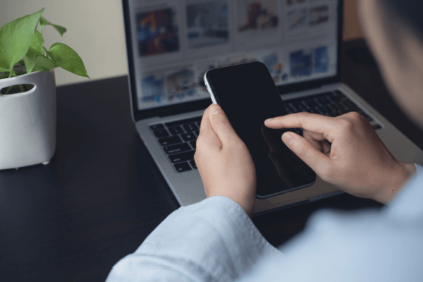 A mobile phone being held above an open laptop with social media images on screen