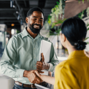 Smiling man holding papers and shaking hands with female in front of him