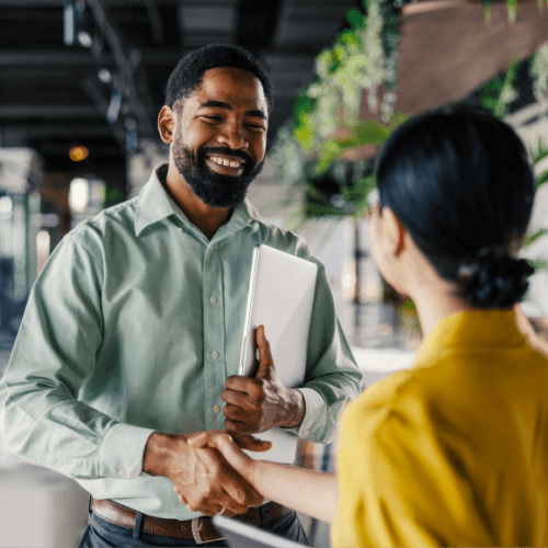 Smiling man holding papers and shaking hands with female in front of him