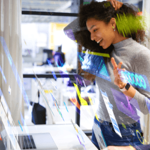 Person smiling while interacting with digital graphics on a transparent display in a modern office.