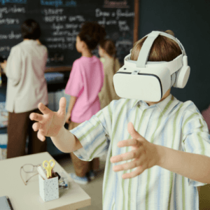 Primary school student wearing a VR headset with teacher and classmates in background at blackboard