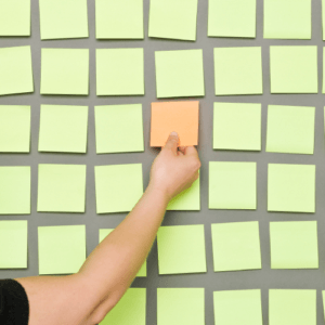 hand places an orange sticky note among a grid of green sticky notes, highlighting a single message standing out from the crowd