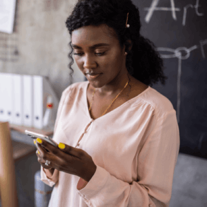 Young female teacher reading emails on her mobile device in her classroom, and considering EdTech purchasing